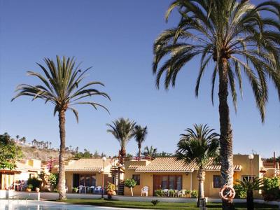 Schwimmbad mit klar blauem Wasser, umgeben von Palmen und gelben Gebäuden unter blauem Himmel.