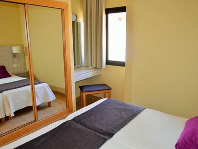 Světý hotelový pokoj s manželskou postelí, velkou zrcadlovou skříní a oknem.