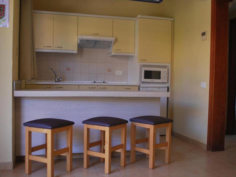 Malá kuchyňka se třemi dřevěnými stoličkami u pultu v hotelovém pokoji.