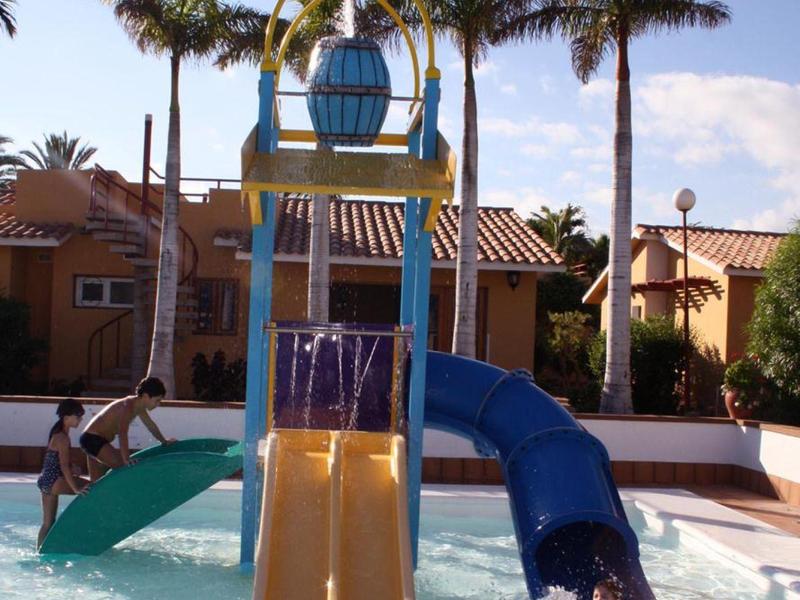 Dětské hřiště se skluzavkou a bazénem pod palmami v hotelové zahradě.