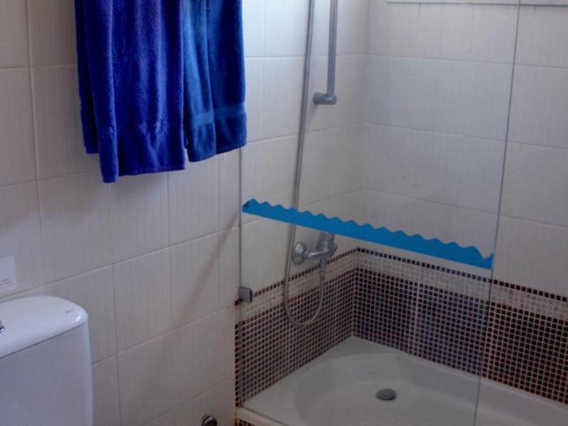 Kompaktní koupelna se sprchou, toaletou, modrými ručníky a malou stoličkou.