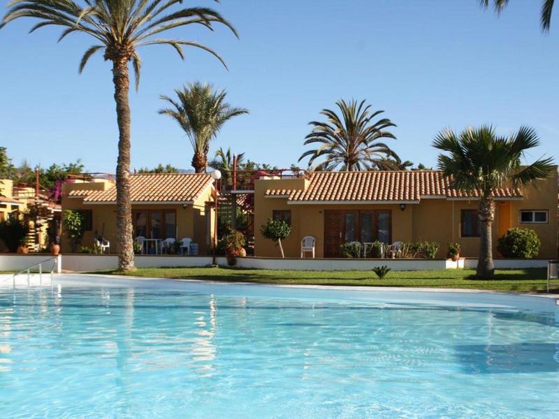 Hotel s velkým bazénem, palmami a bungalovy pod jasnou oblohou