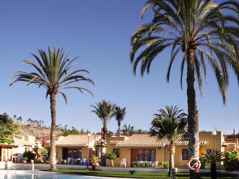 Bazénová oblast s palmami před jednopatrovými hotelovými budovami pod jasnou modrou oblohou