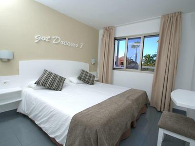 Malý hotelový pokoj s manželskou postelí, dvěma polštáři, oknem a světlými závěsy