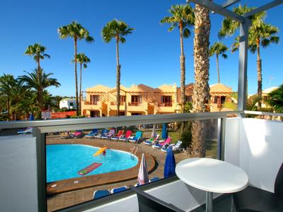 Balkon mit kleinem Tisch und Stuhl, Blick auf Palmen und blauen Pool an sonnigem Tag.