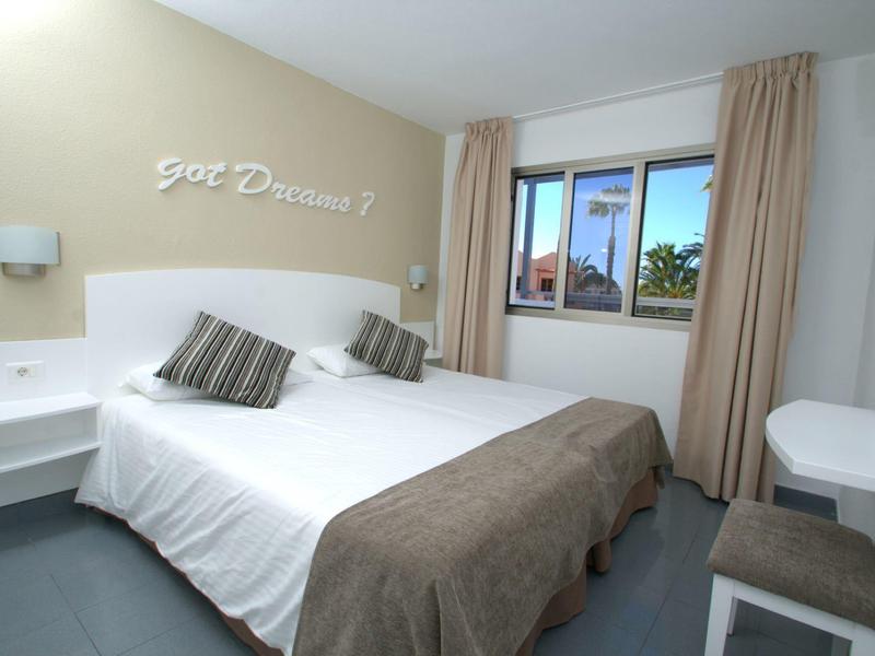 Malý hotelový pokoj s manželskou postelí, dvěma polštáři, oknem a světlými závěsy