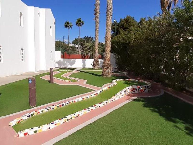 Udržená zahradní cesta s květinami a palmami vedle moderní bílé budovy.