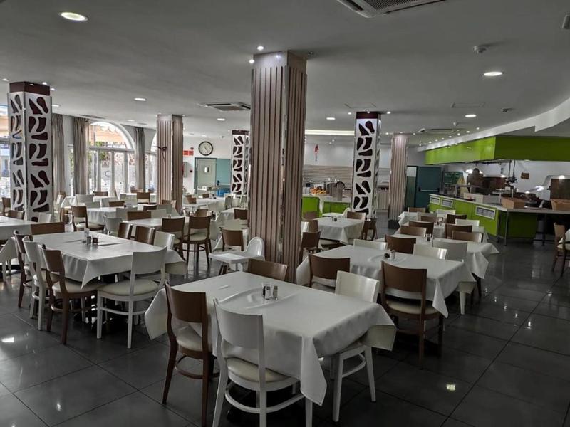 Moderní jídelna s bílými stoly, dřevěnými židlemi a zdobenými sloupy v hotelu.