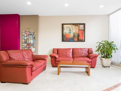 Helles Hotelzimmer mit roten Ledersofas, Holztisch, Pflanze und moderner Wandkunst.