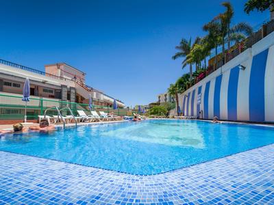 Grande piscine extérieure avec carreaux bleus et chaises longues sous ciel clair.