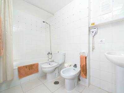 Světlá koupelna s bílými obklady, vanou, toaletou, bidetem a ručníky v jemných barvách.