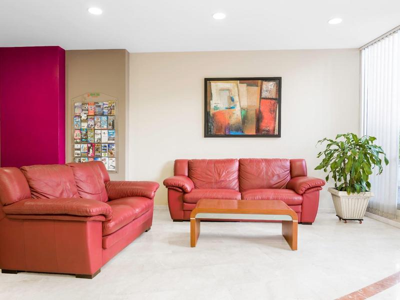 Moderní obývací pokoj se dvěma červenými koženými pohovkami, dřevěným konferenčním stolkem a rostlinami v jasné místnosti.