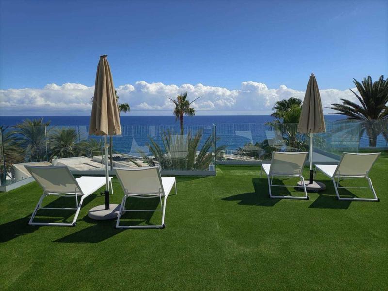 Lounge chairs and umbrellas on a grassy area overlooking the sea under clear skies.