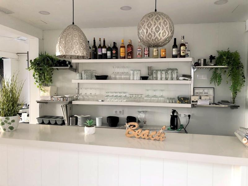 Modern hotel bar with white shelves, plants, and stylish lamps above the counter.