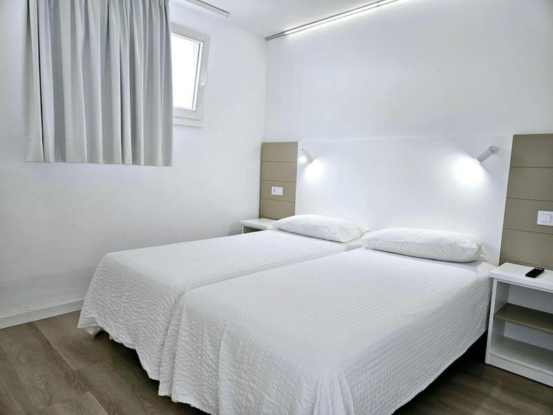 Bright hotel room with two single beds, white bedding, and wooden flooring.