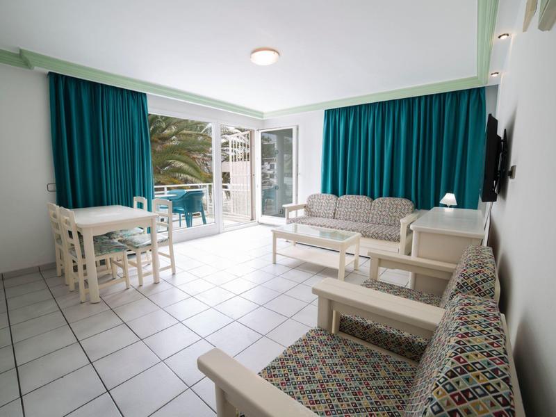 Bright living room with seating, dining table, and balcony view of the sea.