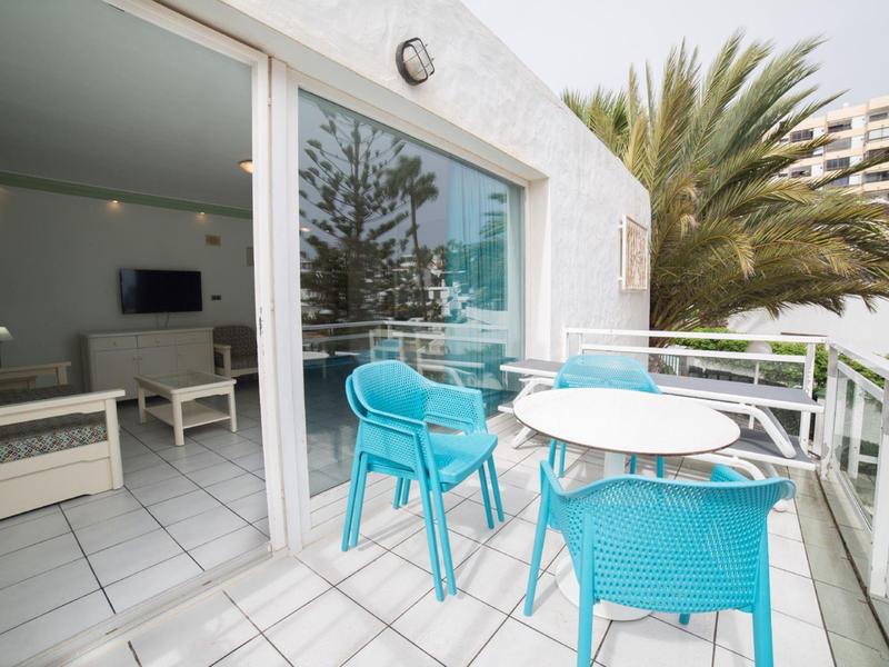 Terrace with white tables and blue chairs at hotel room overlooking palm trees.