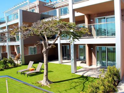 Moderner Hotelkomplex mit Balkonen, Garten und Liegestühlen unter einem kleinen Baum.