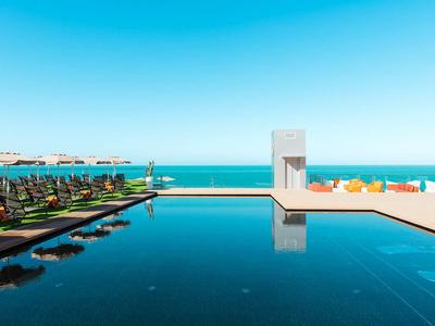 Moderner Infinity-Pool mit Liegestühlen und Meerblick an einem sonnigen Tag.