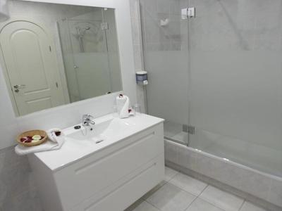 Nowoczesna łazienka hotelowa z białą umywalką, dużym lustrem i szklaną kabiną prysznicową.