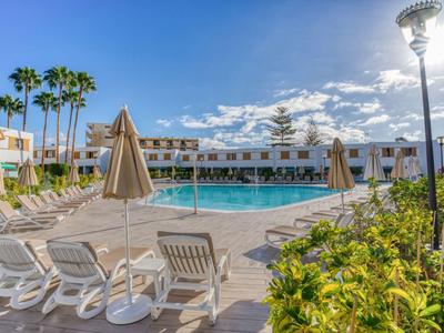 Moderner Hotelpool mit Liegestühlen und Sonnenschirmen unter blauem Himmel.