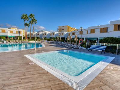 Espace piscine d'hôtel moderne avec petit bassin pour enfants, transats et bâtiments sous un ciel ensoleillé.