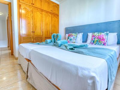 Jasno umeblowana sypialnia z podwójnym łóżkiem, niebieskimi akcentami i dużą drewnianą szafą.