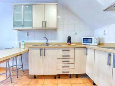 Nowoczesna jasna kuchnia z drewnianymi szafkami, płytkami na podłodze i białymi ścianami.