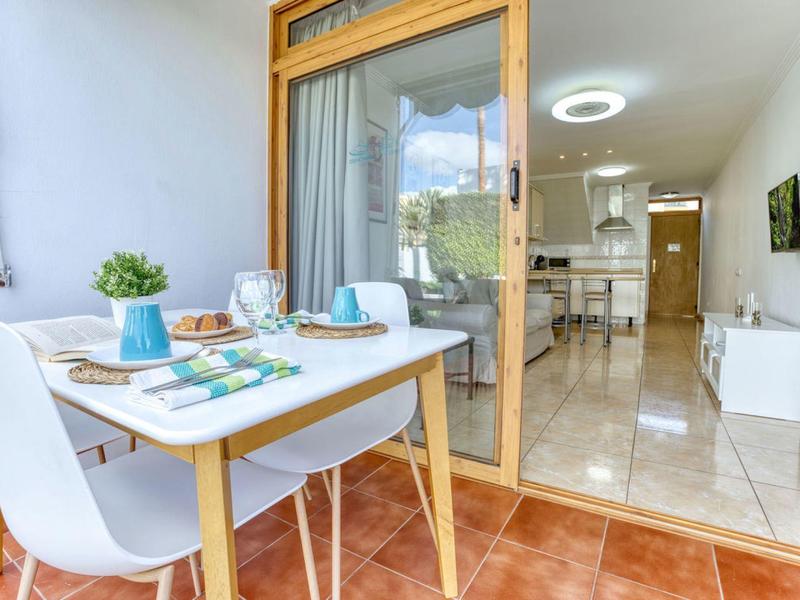 Table de balcon avec deux chaises blanches et table dressée devant porte vitrée ouverte vers l'appartement.