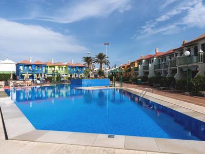 Großer blauer Pool mit Umrandung aus Beton, umgeben von bunten Mehrfamilienhäusern und Palmen.