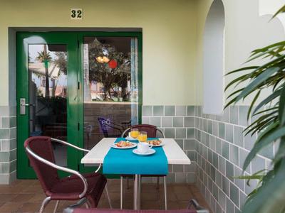 Une table avec un chemin de table bleu dressée pour le petit déjeuner sur un balcon devant des portes doubles vertes.
