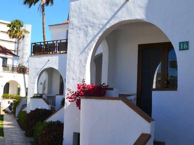 White Mediterranean-style hotel with arches, balcony, palm trees, and vibrant flowers