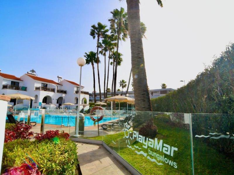 Resort with pool, palm trees, and white buildings under clear blue sky.