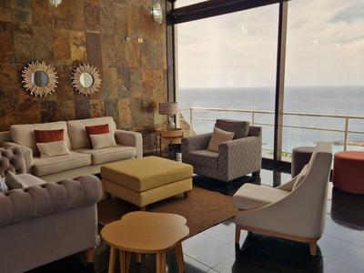 Modern eingerichtetes Wohnzimmer mit Meerblick durch große Fenster und stilvollen Möbeln.