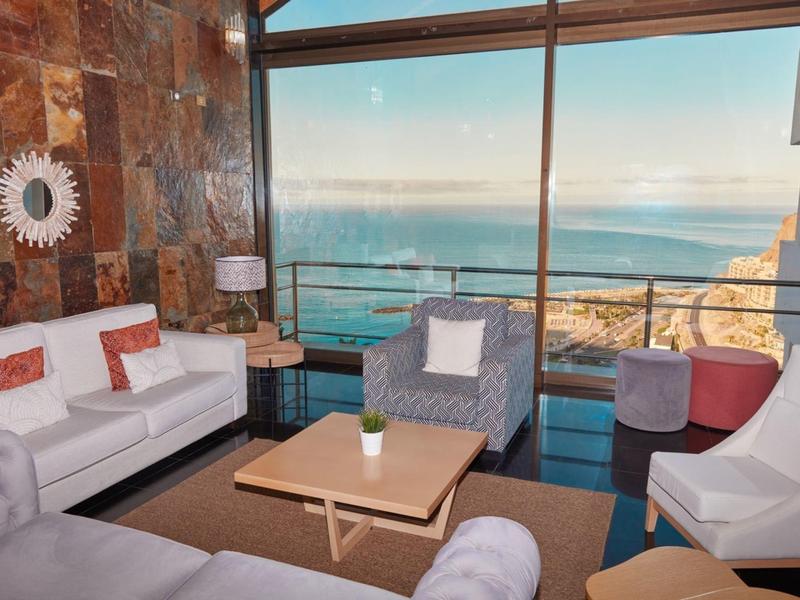 Moderne Wohnzimmerecke mit großen Fenstern, Meerblick, weißen und grauen Sitzmöbeln.