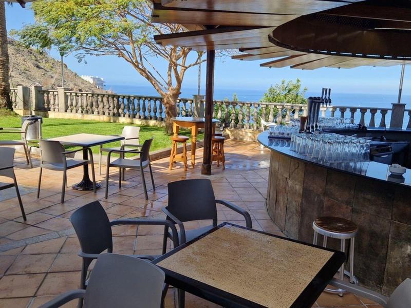 Offene Terrasse mit Tischen, Stühlen, Barbereich und Meerblick im Hintergrund bei Tageslicht.