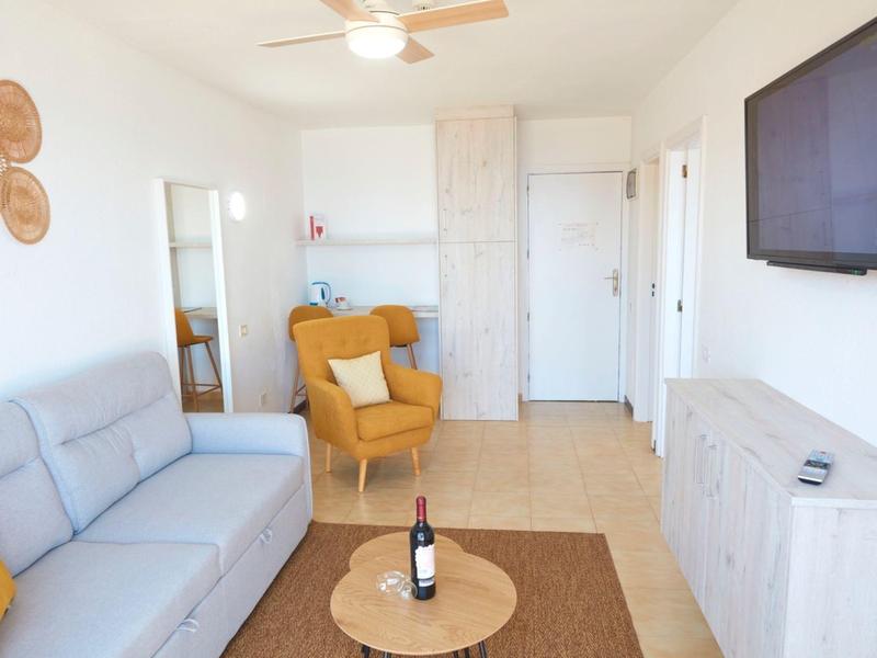 Helles Wohnzimmer mit grauem Sofa, gelbem Sessel, rundem Holztisch und weißem Sideboard.