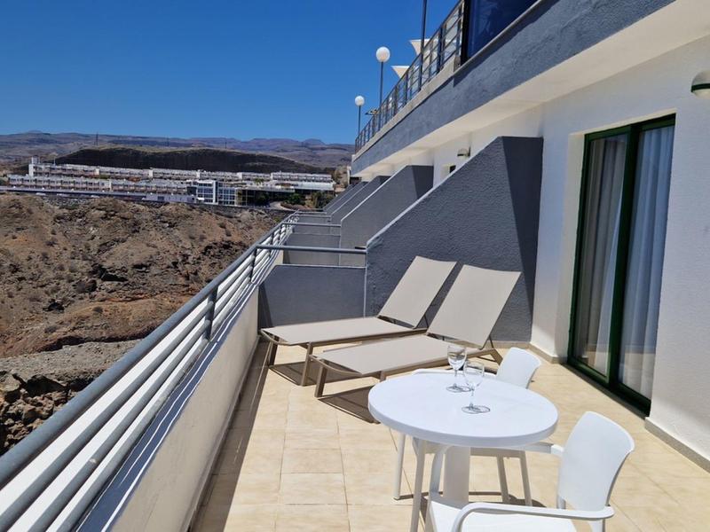 Balkon mit Stühlen und Liegen, Blick auf felsige Landschaft und klares blaues Himmel.