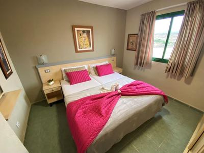 Una camera doppia accogliente con pareti chiare, tappeto verde e accenti rosa sul letto.