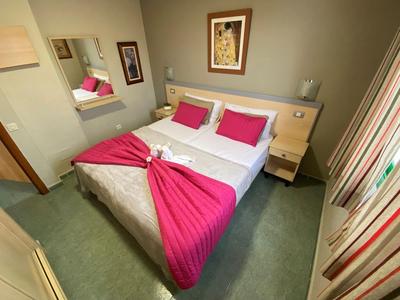 Camera d'hotel accogliente con letto matrimoniale, copriletto e cuscini rosa, moquette verde e quadri alle pareti.