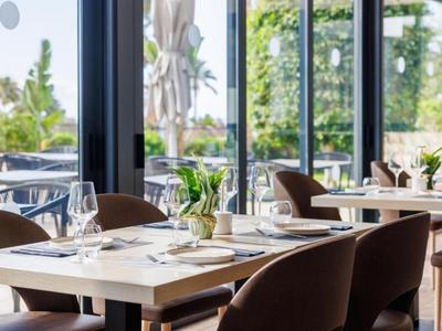 Hell eingerichteter Speisesaal mit gedeckten Tischen und Blick auf eine Terrasse und Garten.