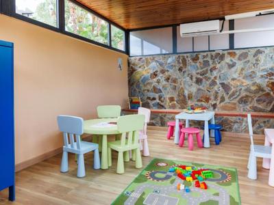 Kinderspielzimmer mit bunten Tischen, Stühlen und Teppich auf Holzboden im Hotelinterieur.