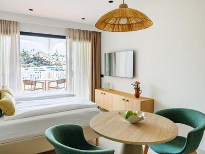 Moderner Hotelzimmerbereich mit Bett, Esstisch, grünen Stühlen und Terrasse mit Stadtblick.