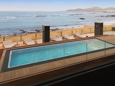 Piscina moderna con ringhiera in vetro che si affaccia sulla costa rocciosa e sul mare sullo sfondo.