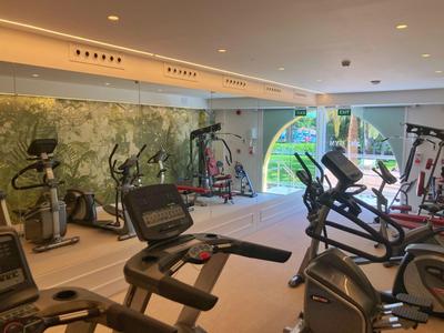 Salle de sport moderne avec tapis de course et équipements, lumineuse grâce aux grandes fenêtres et miroirs.