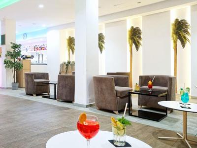 Moderna recepción de hotel con áreas de asiento, mesas blancas y plantas decorativas.