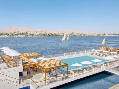 Ein modernes, großes Schwimmbad auf einer Dachterrasse mit Holzliegen und Blick auf einen Fluss.