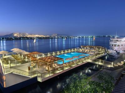 Area piscina illuminata su un hotel galleggiante con vista su una città portuale di notte