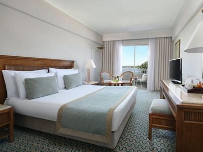 Camera d'hotel luminosa con letto grande, due poltrone e scrivania accanto alla finestra con vista sugli alberi.