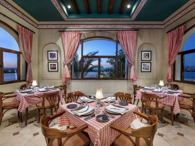 Sala da pranzo elegante con tavoli, tovaglie a quadri rossi e sedie in legno, vista sull'acqua al crepuscolo.